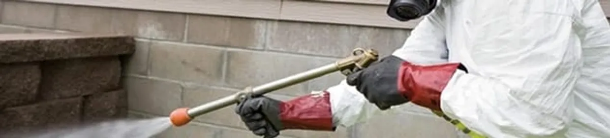 Pest control technician applying exterior insect treatment along a home foundation in Green Bay, WI
