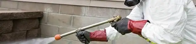 Pest control technician applying exterior insect treatment along a home foundation in Green Bay, WI