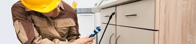 Roach exterminator applying treatment under kitchen cabinets in Green Bay, WI