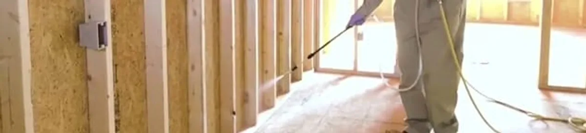 Termite treatment technician applying spray along framing and unfinished walls in Green Bay, WI